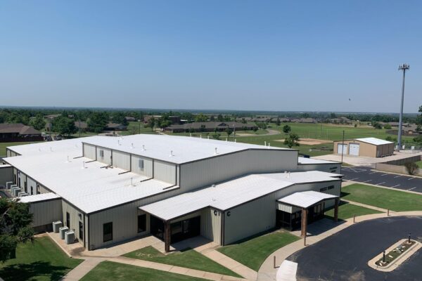 Commercial building with a white roof, surrounded by green grass and clear blue skies, located in Oklahoma, highlighting the importance of durable roofing solutions for local property owners.