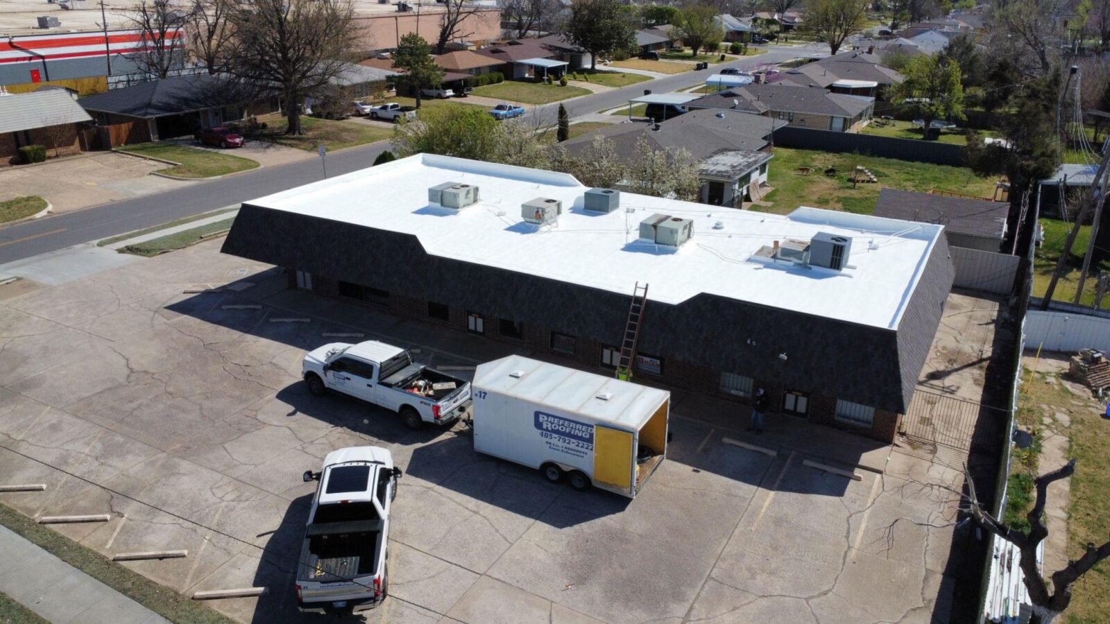 Local roofing contractor building in Oklahoma City with a white roof, parked trucks, and a ladder, illustrating community-focused roofing services.
