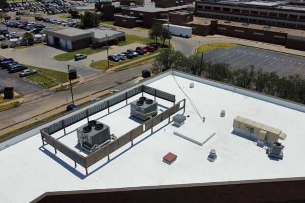 Commercial building rooftop featuring white silicone roof coating, HVAC units, and ventilation systems, relevant to Oklahoma roofing solutions and energy efficiency.