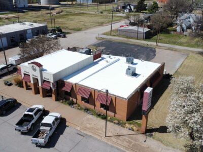 Aerial view of a commercial building with a white cool roof, showcasing energy-efficient roofing options in Oklahoma, surrounded by parking and nearby structures.