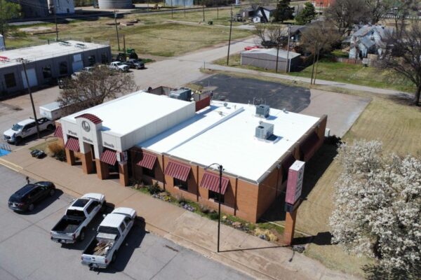 Aerial view of a commercial building with a white cool roofing system, surrounded by vehicles and grass, highlighting energy-efficient roofing solutions for Oklahoma businesses.